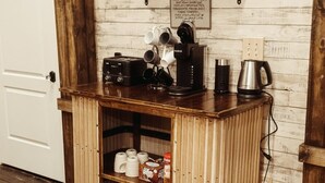 A small wooden kitchenette with a coffee maker, mugs, and a shelf with jars. - The Loft on Main (Belmont)