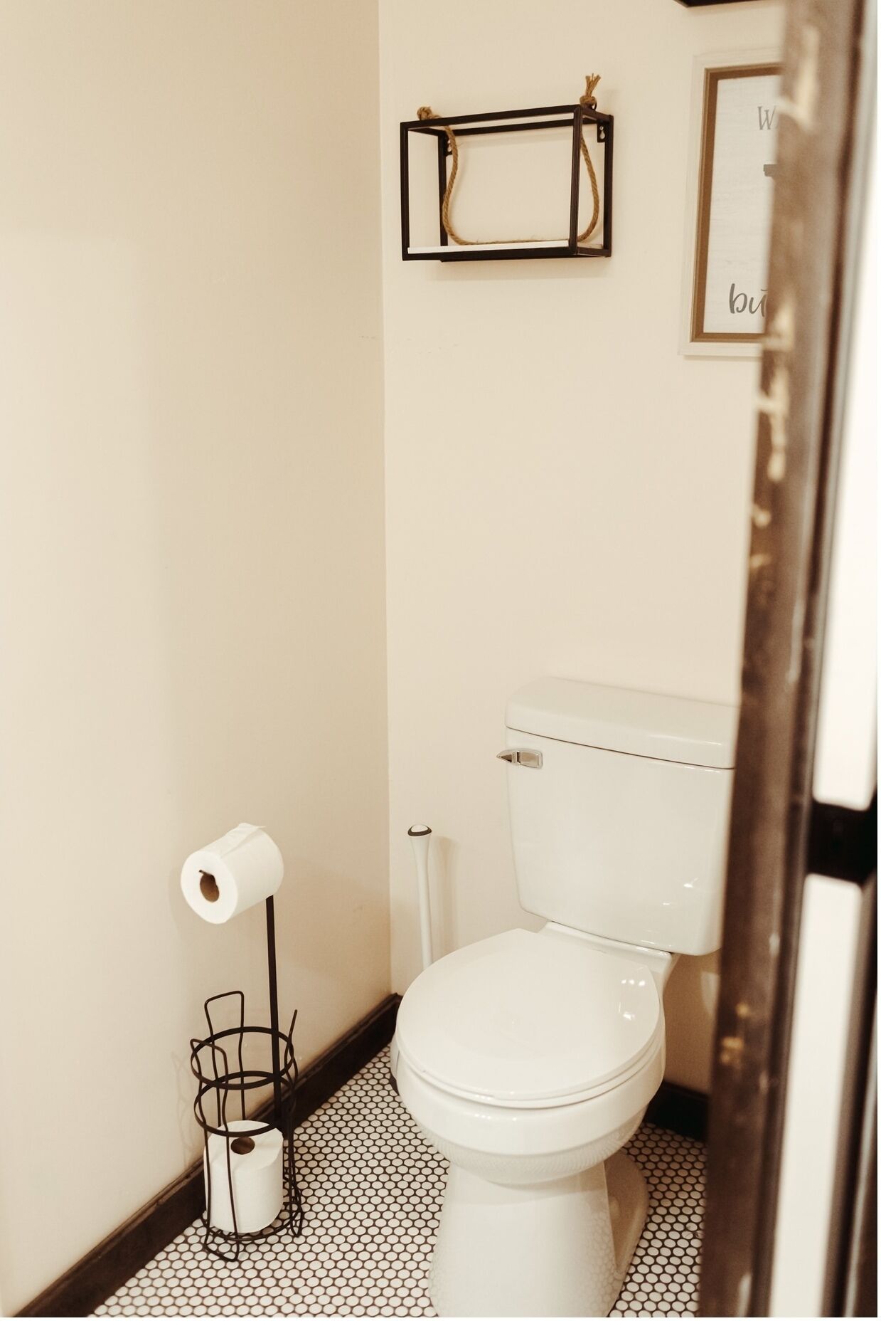 A small bathroom with a toilet, a toilet paper holder, and a framed picture on the wall.