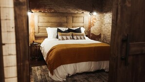 A cozy bedroom with a wooden headboard, a patterned rug, and a warm-toned throw blanket. - The Loft on Main (Belmont)