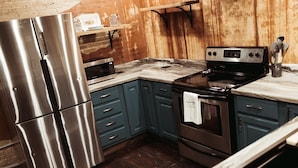 A kitchen with stainless steel appliances, dark blue cabinets, and a wooden wall. - The Loft on Main (Belmont)