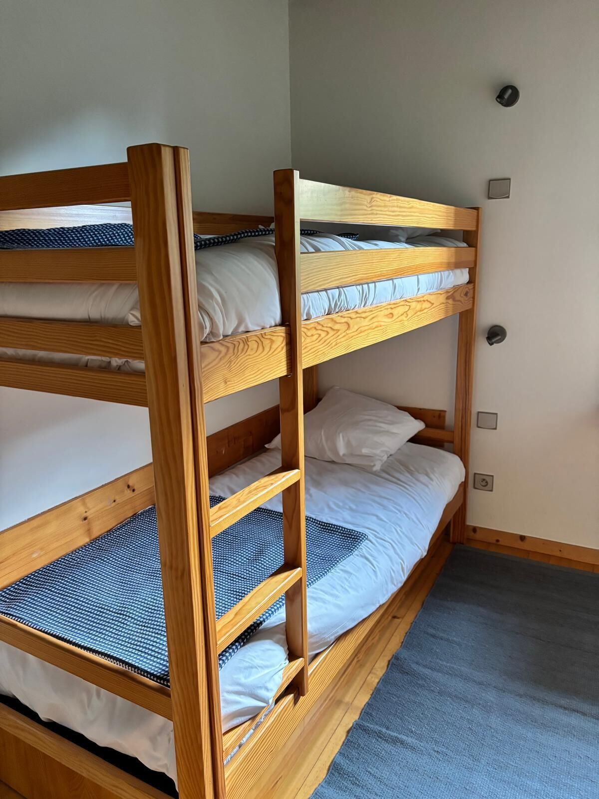 A bunk bed with three levels, wooden frame, and white bedding.
