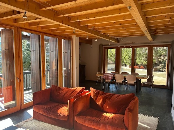 Een ruime woonkamer met houten plafond, grote ramen en een rode bank.