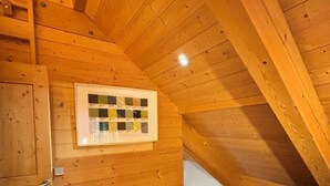 Une petite chambre mansardée aux murs en bois, avec un lit simple, une fenêtre et un nuancier encadré accroché au mur.
