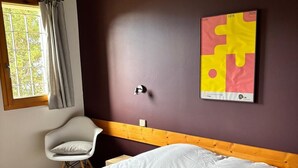 Une chambre à coucher avec un lit, une chaise, une fenêtre avec des rideaux et un mur orné d’une œuvre d’art représentant un élément de puzzle.