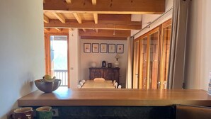 Une cuisine avec un long comptoir en bois, une table à manger et un réfrigérateur. On y trouve deux tasses sur le comptoir et un bol rempli de citrons.