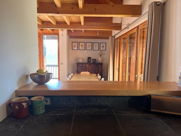 A kitchen with a long wooden countertop, a dining table, and a refrigerator. There are two mugs on the counter and a bowl with lemons. - Chalet D'architecte - Domaine Alpe D'huez - 9 Personnes (Villard-Reculas)