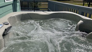 A hot tub with water bubbling, a metal railing, and a house in the background.