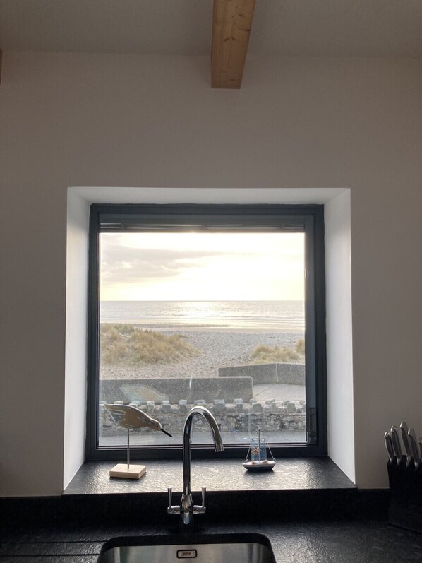 A kitchen with a window overlooking a beach, a modern faucet, and a knife block.