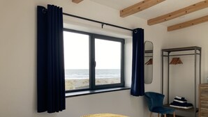 A bedroom with a bed, a chair, a wardrobe, and a window with curtains. - Beach Haven (Hafan y Traeth)  (Barmouth)