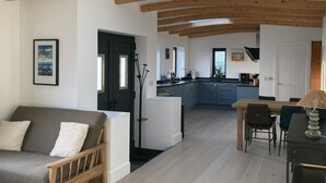 A modern interior with exposed wooden beams, a kitchen with blue cabinets, a dining area with a table and chairs, and a sofa with decorative pillows. - Beach Haven (Hafan y Traeth)  (Barmouth)