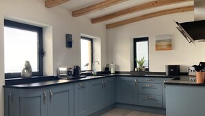 A modern kitchen with blue cabinets, a wooden ceiling, and a large window providing natural light. - Beach Haven (Hafan y Traeth)  (Barmouth)