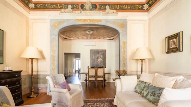 A spacious living room with a high ceiling, ornate ceiling decorations, a dining area with a painting, and a view into another room. - Lusso e Charme
Wonderful apartment in the city center of Florence! (Firenze)