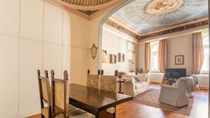 A spacious room with a dining area featuring a wooden table and chairs, a living area with a sofa and armchairs, and a ceiling with intricate artwork. - Lusso e Charme
Wonderful apartment in the city center of Florence! (Firenze)
