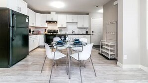 A modern kitchen with white cabinets, a black refrigerator, and a dining table set with blue bowls and glasses. - Bright Spacious Suite - King Bed - Long Stays - WiFi
 (Edmonton)