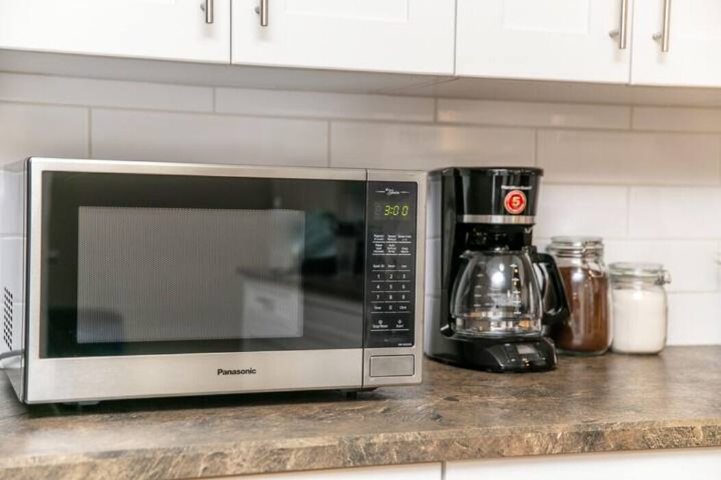 Une cuisine équipée d’un four à micro-ondes, d’une machine à café et de pots disposés sur le plan de travail.