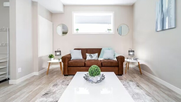 A modern living room with a brown sofa, a white coffee table with a plant, and a large window. - Bright Spacious Suite - King Bed - Long Stays - WiFi
 (Edmonton)