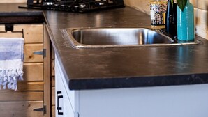 A kitchen with wooden walls, a stainless steel sink, a kettle, and a gas stove. - Tiny A-Frame Cabin with Outdoor Fire Pit! (Sunset House)