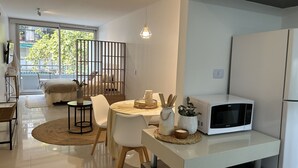 A modern kitchen with a white microwave, a dining table with chairs, and a large window with a view of greenery outside. - CloudBA Guemes Soho Apartments (Buenos Aires)
