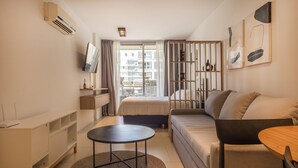 A modern, well-lit bedroom with a bed, a sofa, a small table, and a TV. - CloudBA Guemes Soho Apartments (Buenos Aires)
