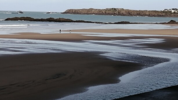 A beach with a rocky shoreline, calm water, and a person walking. - Appartement rez -de Chaussée en Centre Ville (Dol-de-Bretagne)