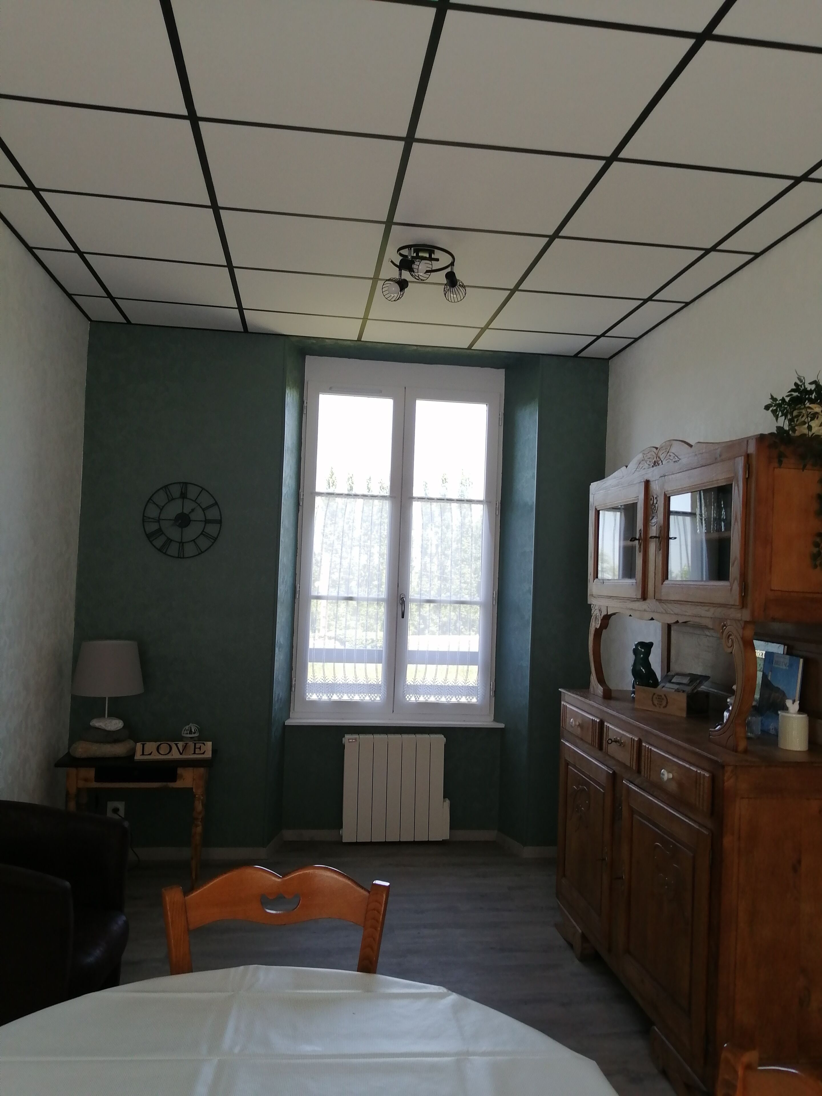A room with a large window, a wooden cabinet, a clock, and a table.