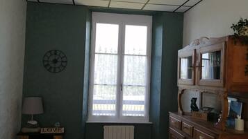 A room with a large window, a wooden cabinet, a clock, and a table.