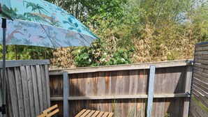 A wooden table and bench set in a garden with a wooden fence and a colorful umbrella. - Appartement rez -de Chaussée en Centre Ville (Dol-de-Bretagne)