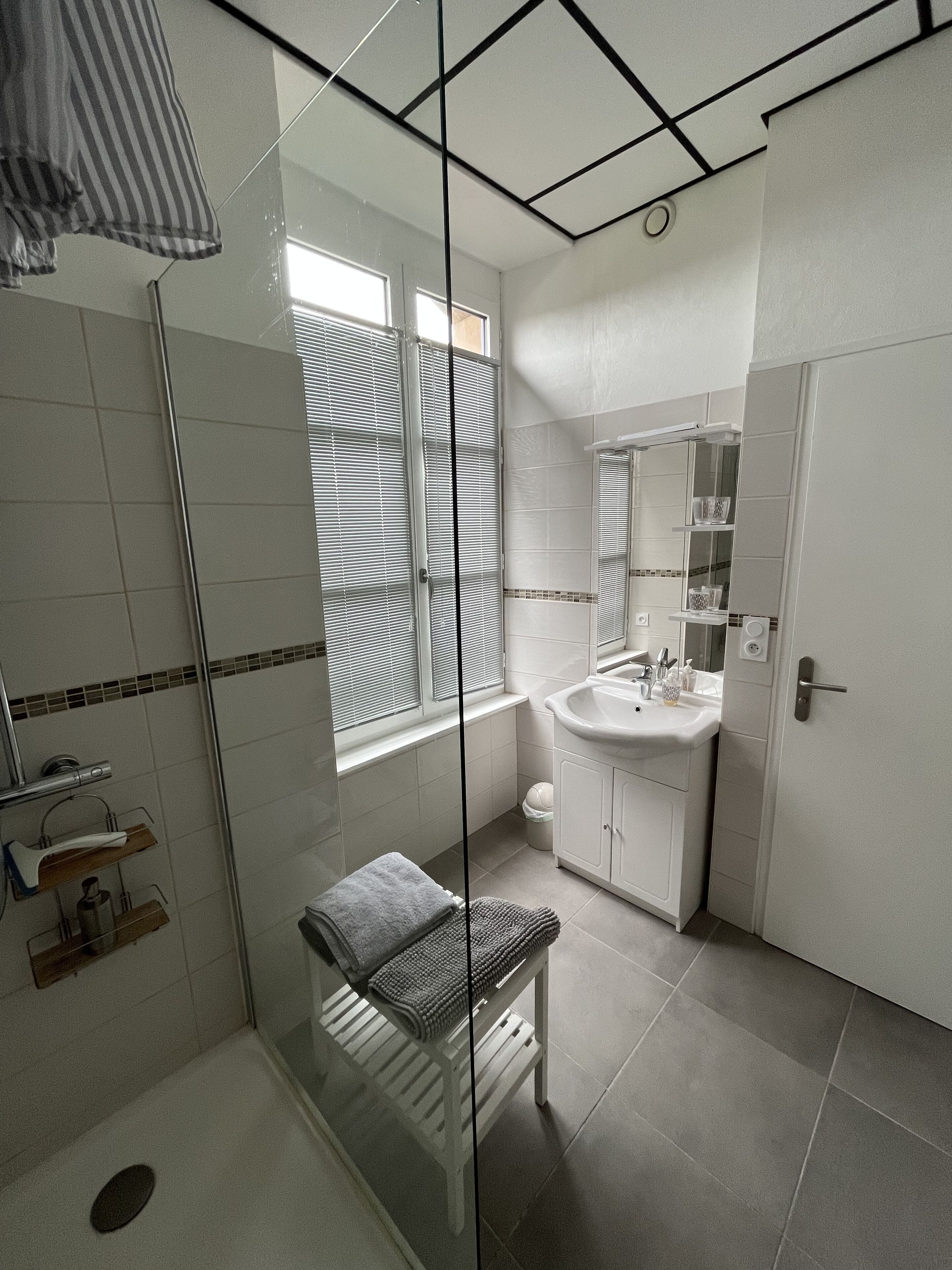 Un bagno moderno con cabina doccia in vetro, lavabo bianco e una panca.