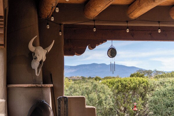 Un interior rústico con una decoración de cráneo de toro, un móvil colgante y vistas a montañas y follaje en el exterior.