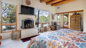A bedroom with a large bed, a fireplace, a TV, and a view of the outdoors.