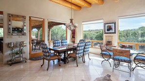 A spacious dining area with a wooden ceiling, large windows offering a view of the outdoors, and a variety of seating options including checkered chairs and wicker chairs.