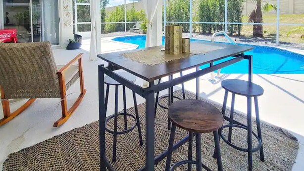 A covered outdoor area with a pool, a table, and two bar stools. - The Art House @ Walt Disney (Davenport)