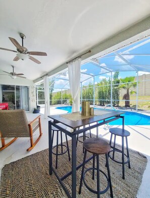 A covered outdoor area with a pool, a table, and two bar stools.