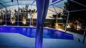 A swimming pool with a clear blue water feature, surrounded by a covered area with a view of trees and a sunset. - The Art House @ Walt Disney (Davenport)