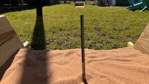 Un patio trasero con un arenero, una estructura de juego de madera y una casita de juegos azul.