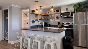 Una cocina moderna con una isla central, taburetes de bar, electrodomésticos de acero inoxidable y decoración en la pared.