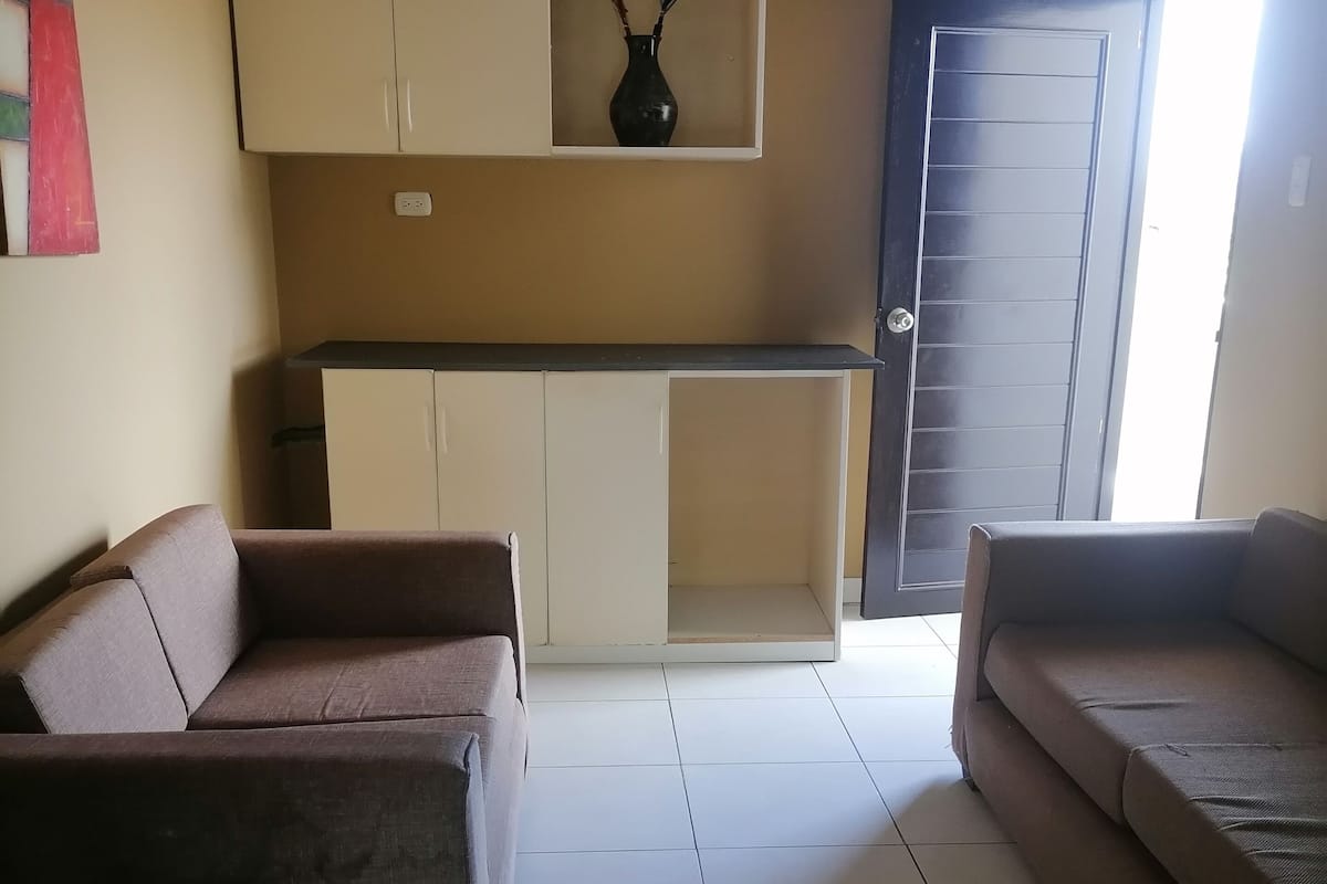 A living room with two sofas, a kitchen area with cabinets, and a door leading outside.