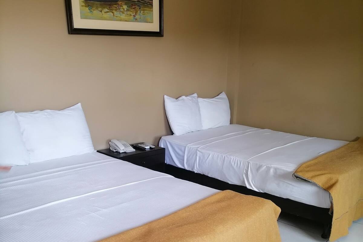 A hotel room with two beds, a painting on the wall, and a tiled floor.