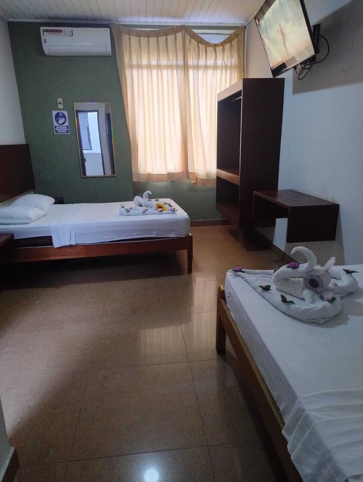 Habitación de hotel con dos camas individuales, televisión, espejo y ventana con cortinas.