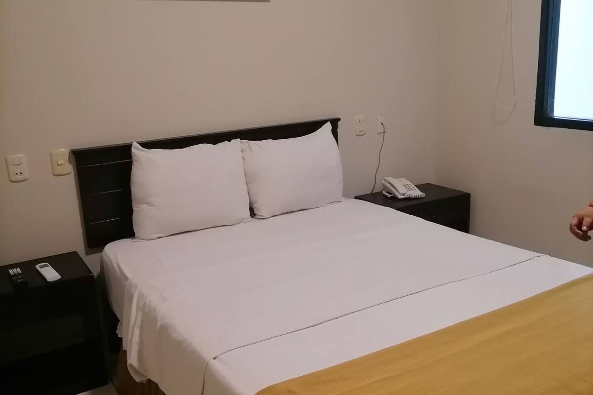 A hotel room with a bed, a nightstand, a phone, and a painting on the wall.