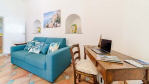 A cozy living room with a blue sofa, a wooden desk with a laptop, and a chair with a white cushion. - Romantic Antica Sponda (Positano)