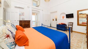 A bedroom with a bed, a dresser, a chair, a television, and a window with curtains. - Romantic Antica Sponda (Positano)