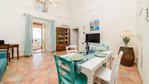 A dining area with a white table, green chairs, and a tiled floor. There is a wooden cabinet and a television on the wall. - Romantic Antica Sponda (Positano)