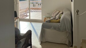 Une chambre avec un lit, une chaise en osier, une petite table et une vue sur un balcon doté d’une balustrade.