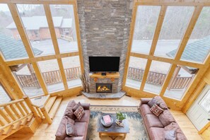 A cozy room with a stone fireplace, wooden furniture, and large windows. - Morven by Avantstay Secluded w/ Mountain Views! (Sevierville)