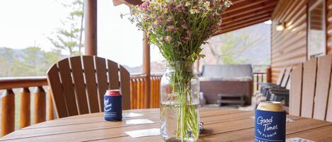 A wooden table with a glass vase of flowers, two cans of beer, and playing cards.