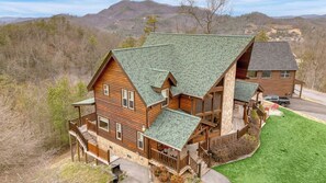 A log cabin with a green roof, a deck, and a stone foundation. - Morven by Avantstay Secluded w/ Mountain Views! (Sevierville)