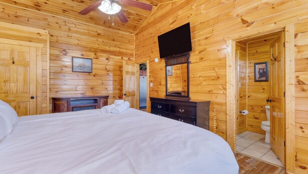 Een slaapkamer in een houten chalet met een bed, een kapstok, een spiegel en een plafondventilator.