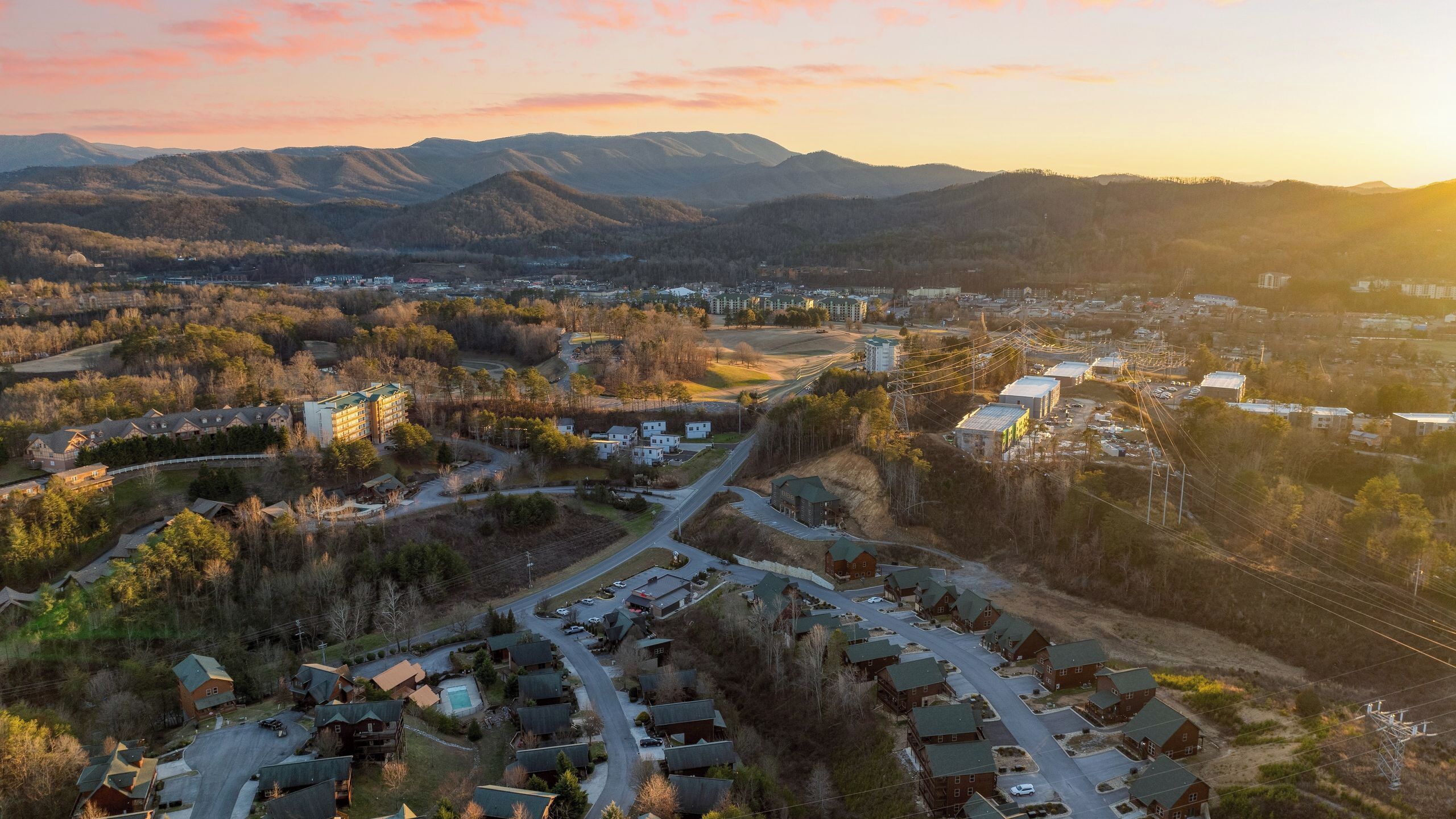 An aerial view of a residential area with a mix of single-family homes and apartment buildings, surrounded by hills and a clear sky.