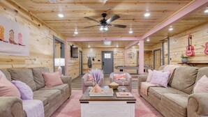 A cozy, well-lit room with wooden walls and ceiling, featuring two sofas, a coffee table, and a ceiling fan. - Pink Pines by Avantstay Luxury Aesthetic Dream Home, Indoor Pool, Hot Tub (Sevierville)